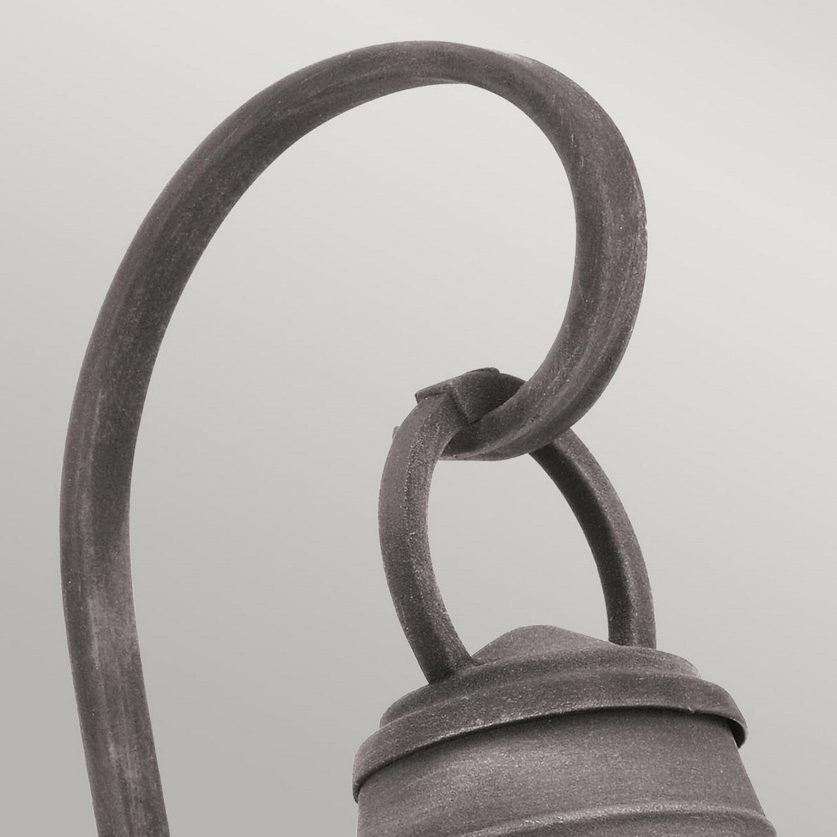 Close-up of the Bridgepoint Outdoor 1 Light Small Wall Lantern in weathered zinc, elegantly supported by a curved metal hook against a light gray background. The design showcases smooth, flowing lines with seeded glass that adds rustic charm.