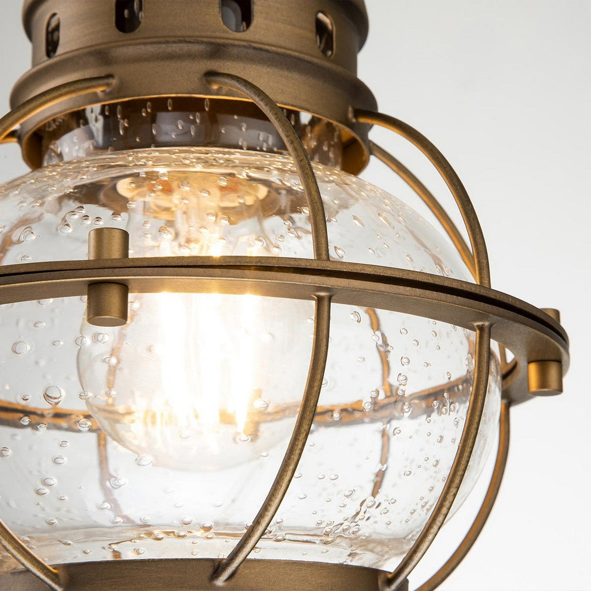A close-up of the Bridgepoint Outdoor 1 Light Small Chain Lantern in natural brass features a bubbled, seeded glass globe. The illuminated bulb inside emits a warm glow, enhancing its timeless charm.