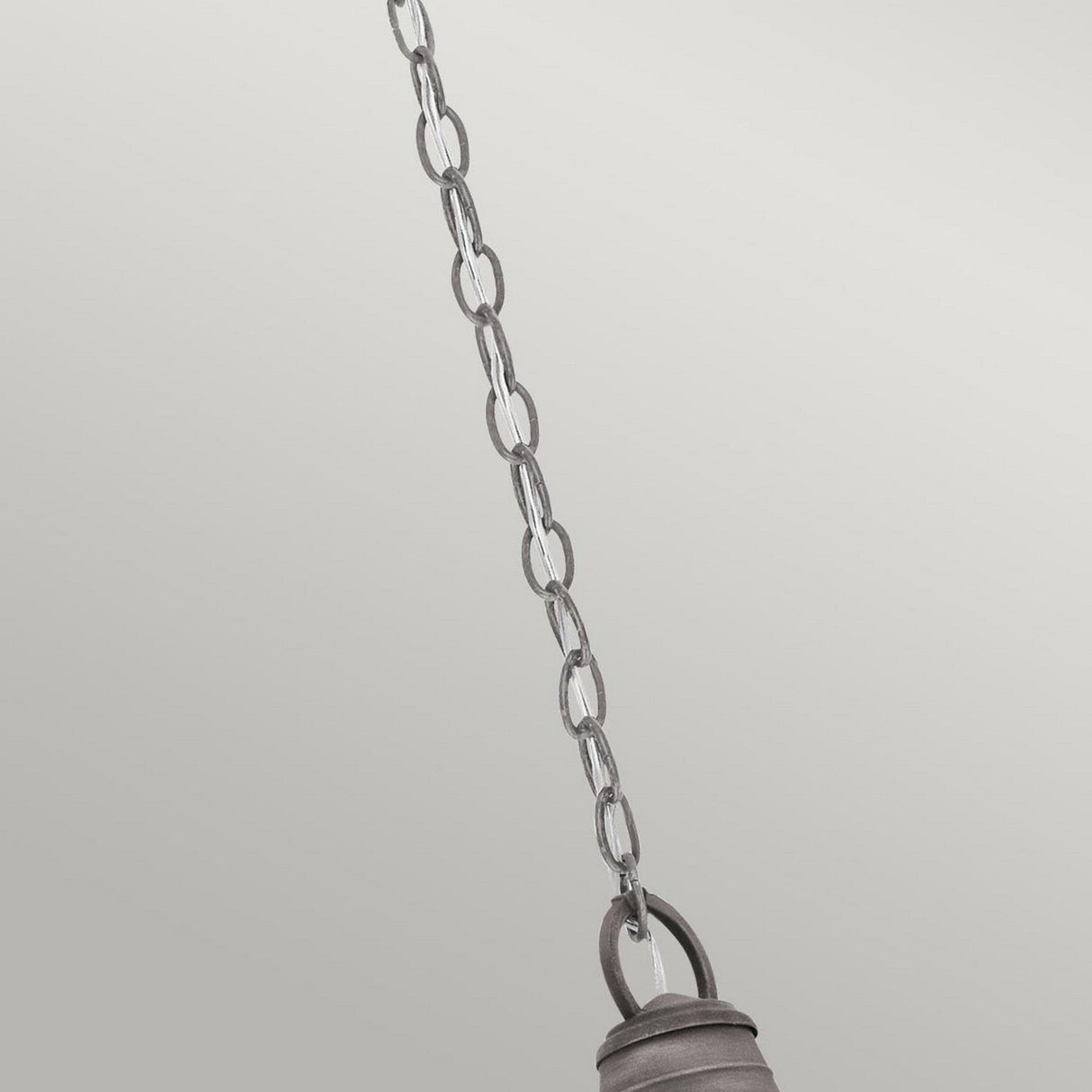 A detailed view of the Bridge Point Outdoor 1 Light Small Chain Light in weathered zinc, set against a light gray background. The chain is connected to an unseen fixture, showcasing a section of a metallic ring at the bottom that captures the rustic charm of an outdoor lantern.