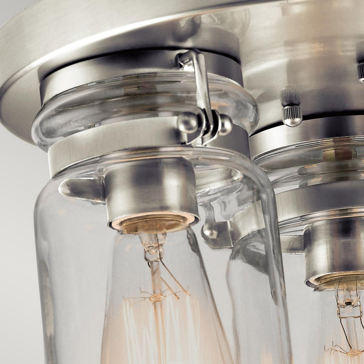 Close-up of the Brinley 3 Light Flush with a brushed nickel finish, featuring clear glass shades and a vintage-style exposed filament bulb. The design beautifully highlights industrial and modern aesthetics.
