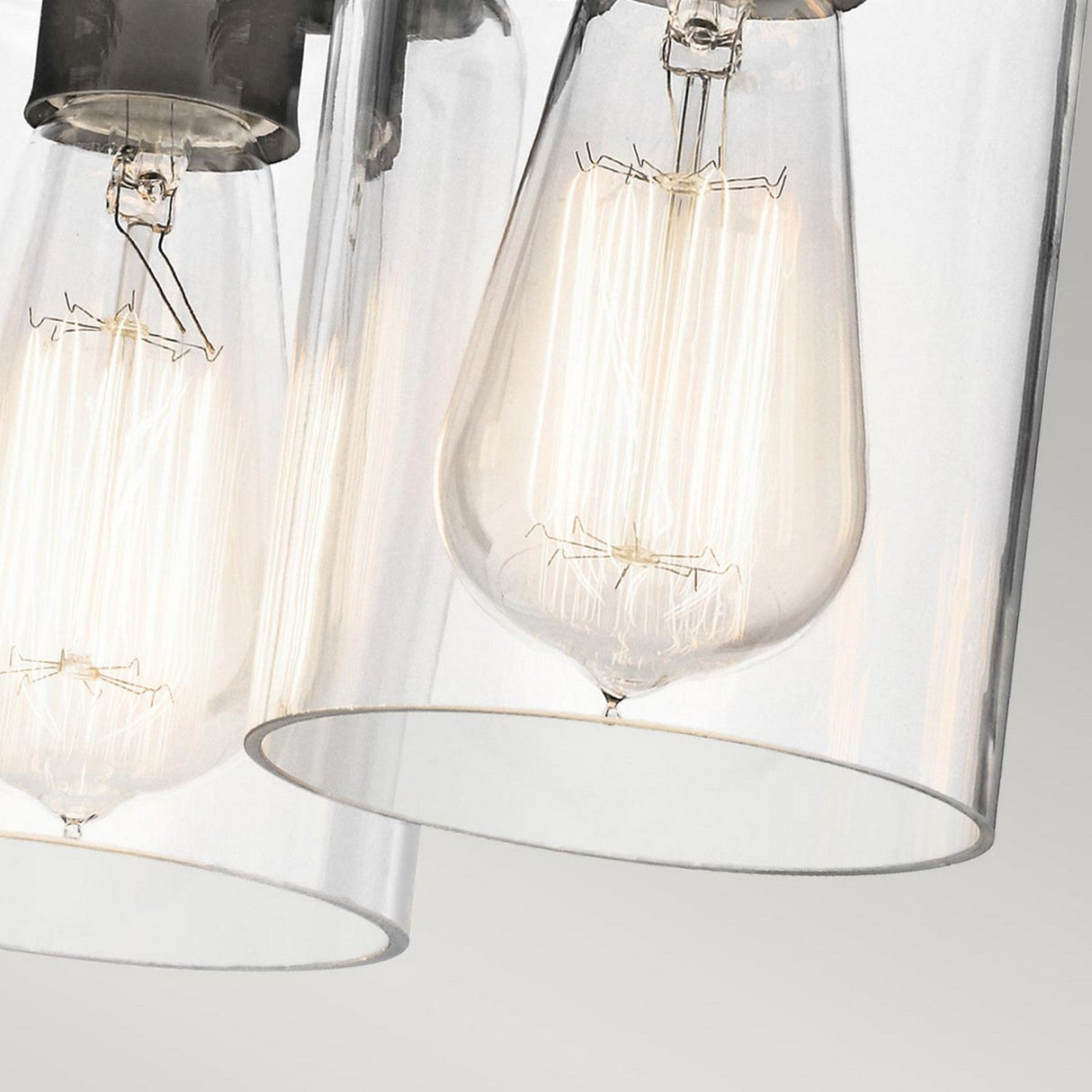 Close-up of two illuminated bulbs from the Brinley 3 Light Flush - Bronze, featuring a vintage-inspired design encased in clear glass shades and cylindrical fixtures, set against a light gray background.