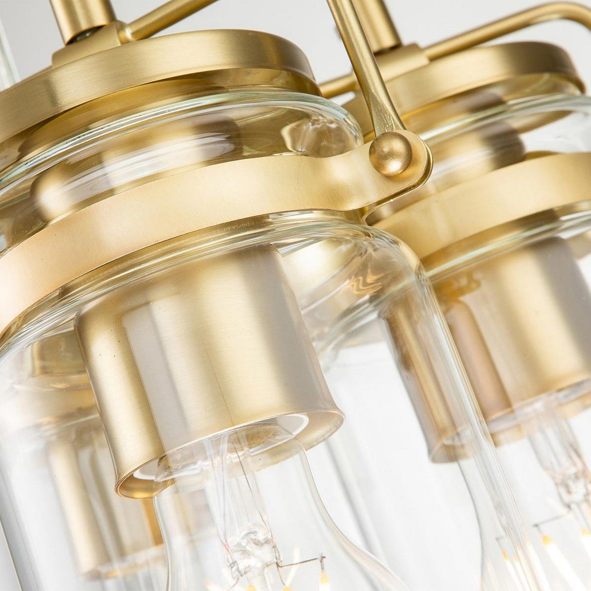 A close-up of the Brinley 3 Light Pendant - Brushed Brass showcases its clear cylindrical glass shades and elegant brushed brass touches. The design highlights exposed light bulbs, while the polished brass finish adds a modern and sophisticated look to the fixture.