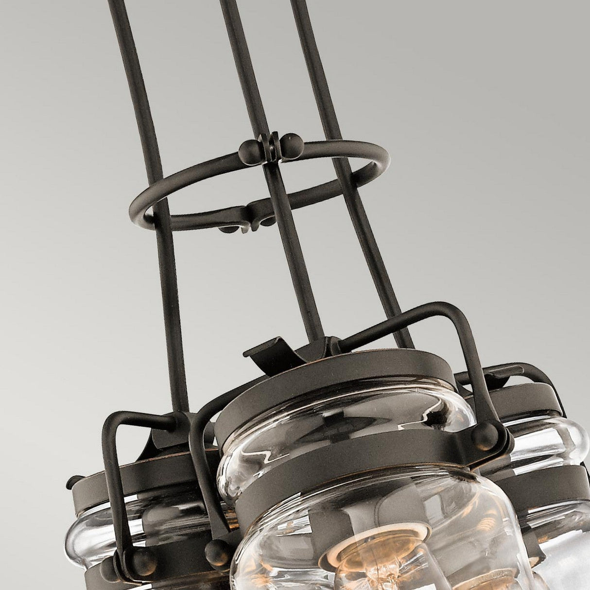 Close-up of the Brinley 3 Light Pendant in Bronze, showcasing its modern industrial style with black metal fixtures and clear glass shades. This chandelier features multiple suspended lamps, blending vintage charm with a sleek and contemporary design against a neutral background.