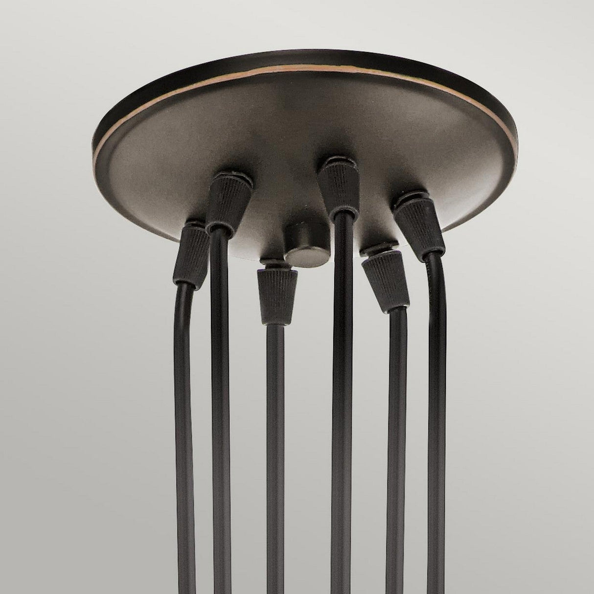 A close-up of the Brinley 6 Light Pendant - Bronze reveals its vintage-inspired finish with six black cables extending downward. This ceiling mount features a smooth, metallic texture and a minimalistic design set against a light gray background.