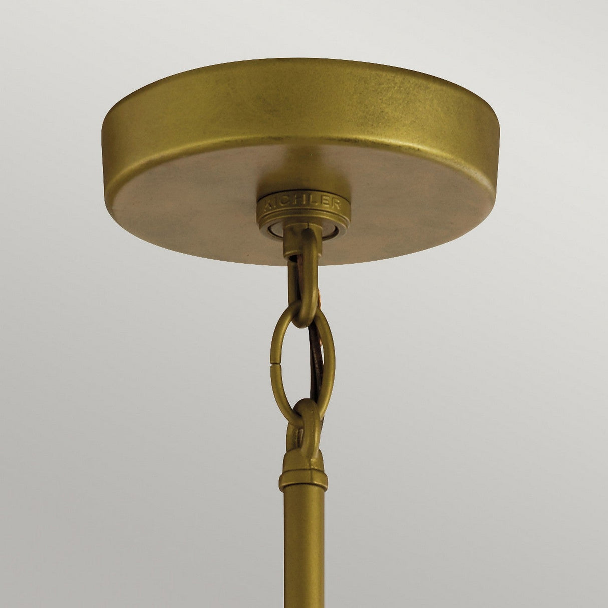 A close-up of the Camillo Outdoor 1 Light Outdoor Pendant in natural brass highlights its round ceiling mount and central rod, elegantly connected with a decorative chain link. This minimalist design is set against a plain background, beautifully complemented by clear seeded glass elements.