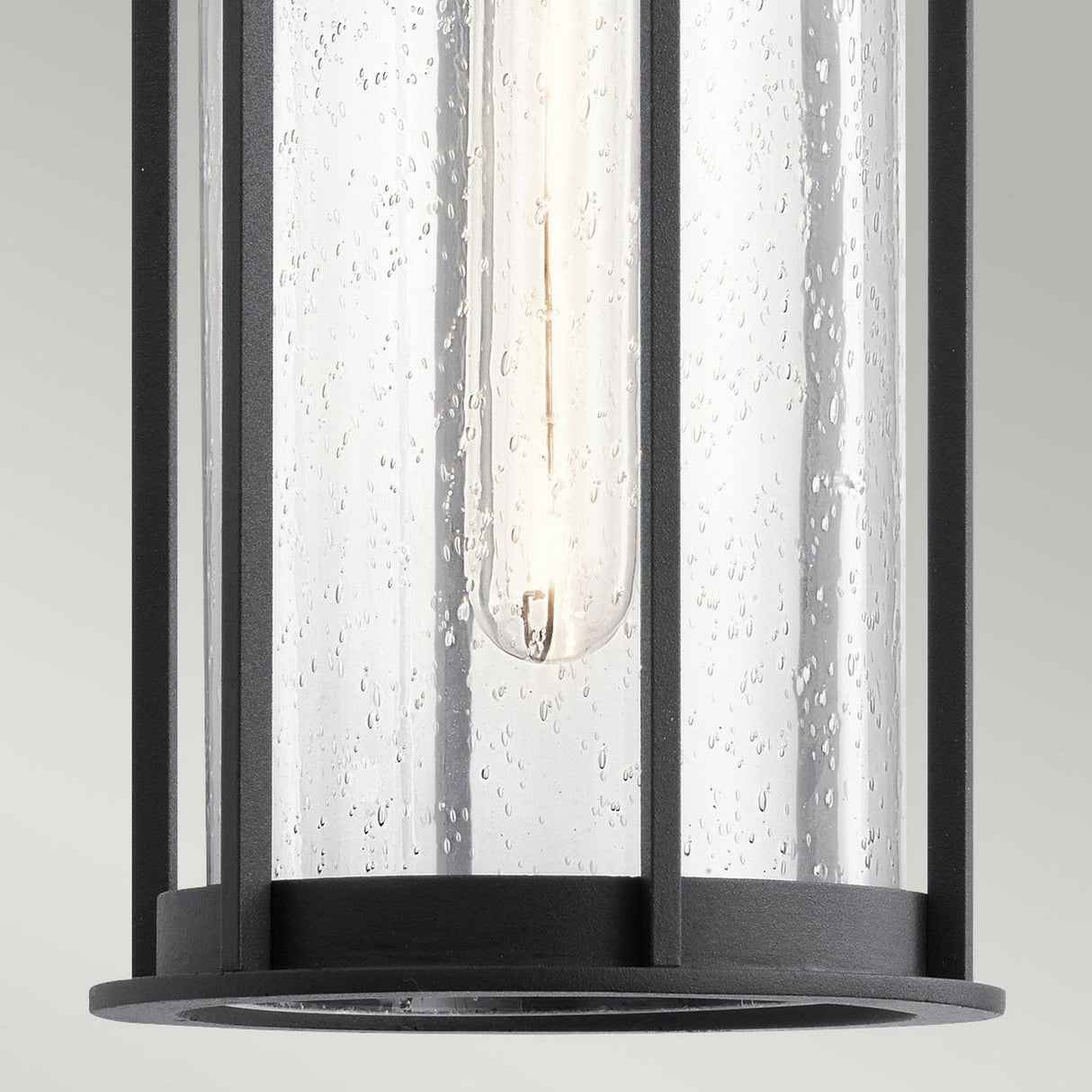 Close-up of the Camillo Outdoor 1 Light Pendant in black, featuring a transparent seeded glass cover. The visible bulb inside emits a soft glow that enhances the fixture's sleek finish.