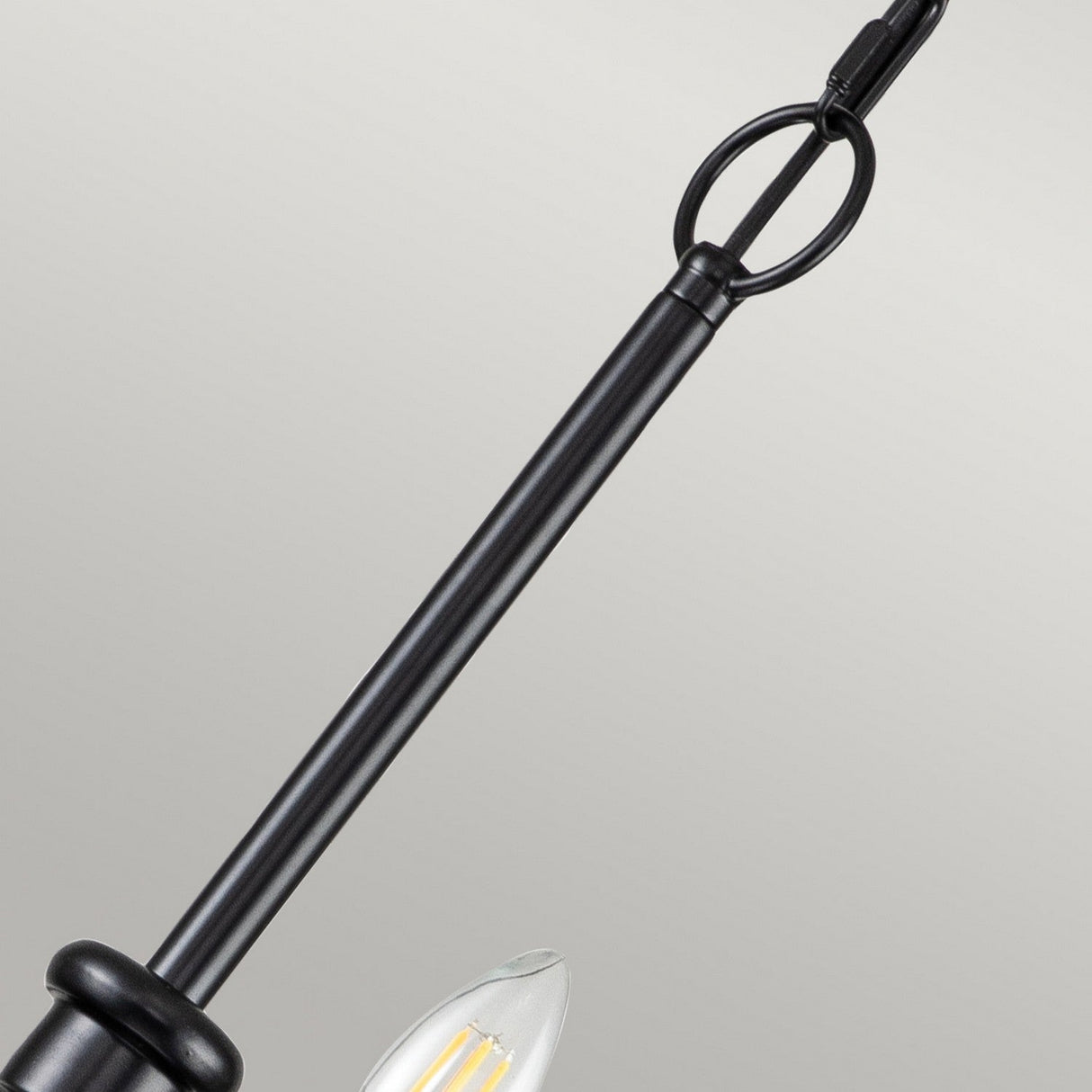 Close-up of the Capitol Hill 12 Light Chandelier - Black, showcasing its black metal frame with a single candle-shaped LED bulb. The elegant design includes a round ring for hanging and is set against a plain gray background.