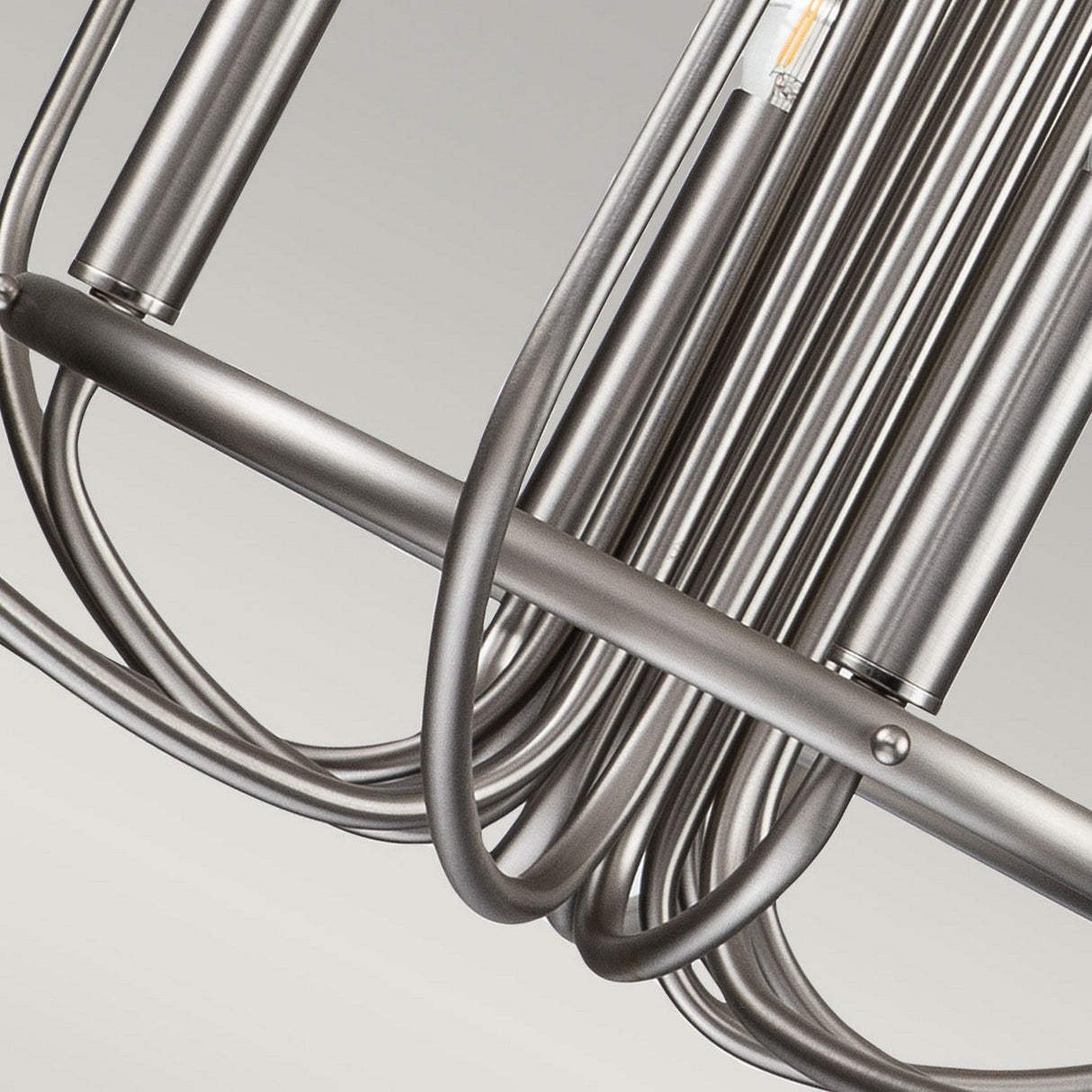 Close-up of the Capitol Hill 12 Light Chandelier - Brushed Nickel, showcasing its modern metallic design with cylindrical shapes and curved rods that produce an industrial aesthetic. The brushed nickel finish enhances its minimalist style, bringing sophistication and elegance.
