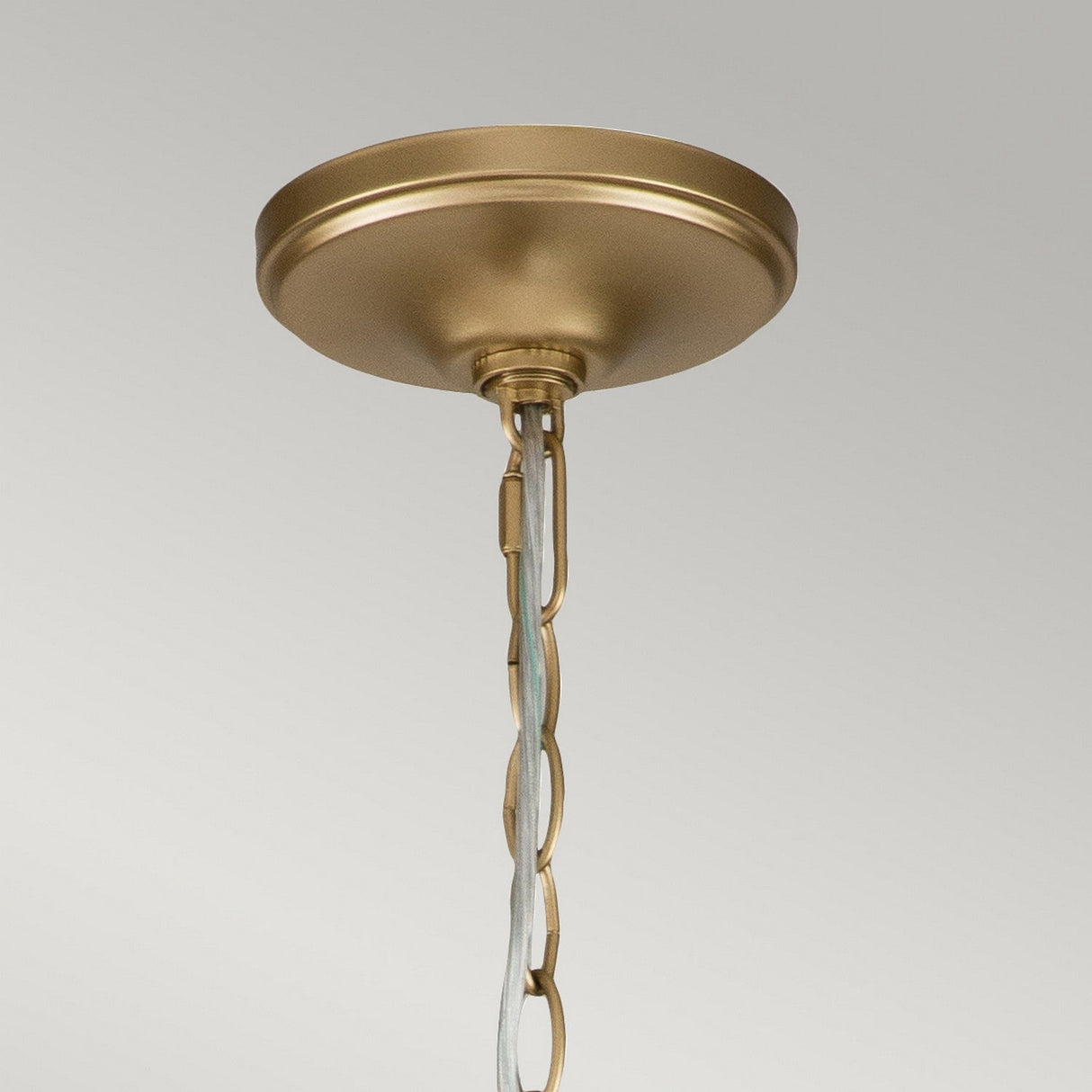 A detailed view of the Capitol Hill 12 Light Chandelier - Brass reveals its classic design, with a decorative chain hanging down. The light gleams off its elegant twelve-arm structure against the plain light gray backdrop.