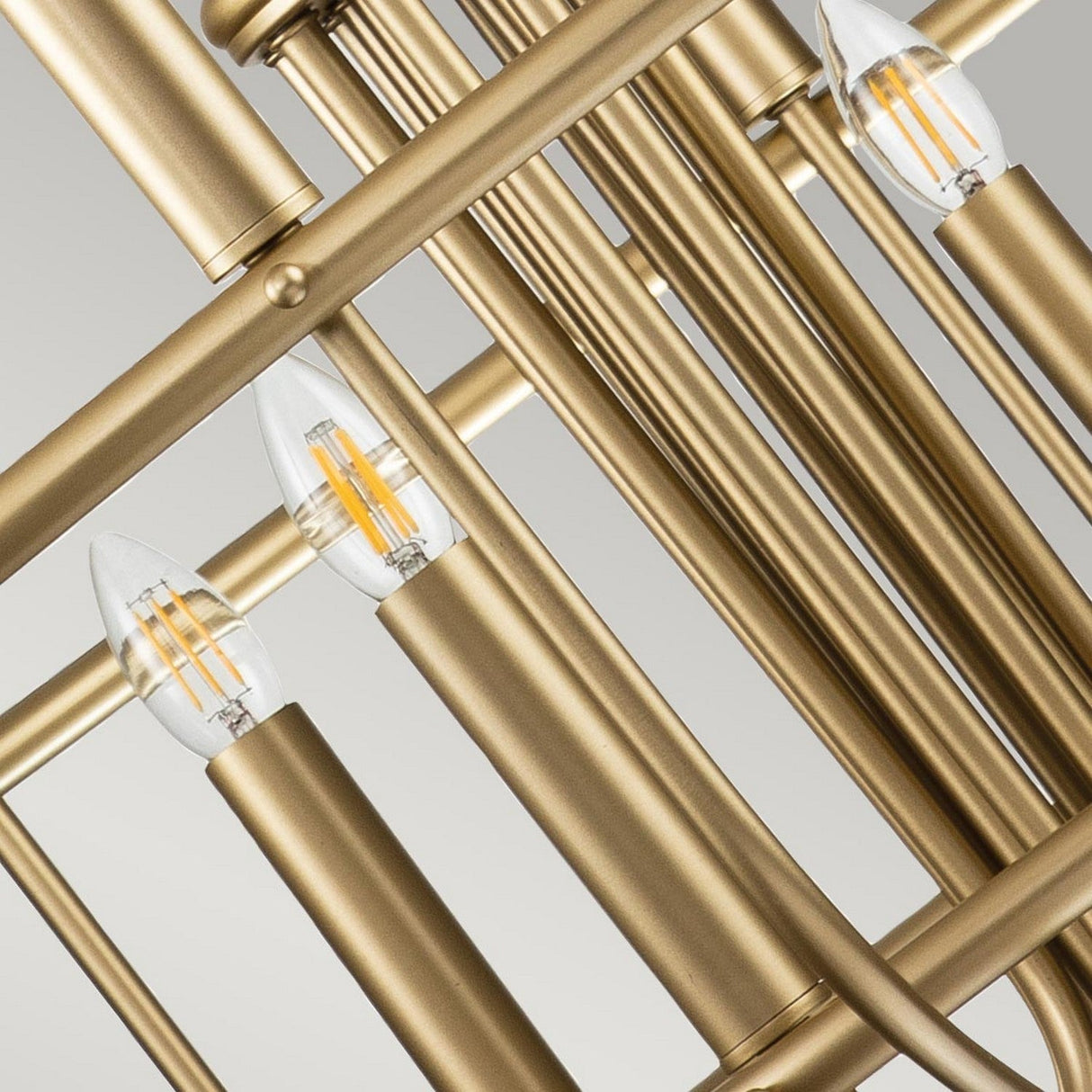 Close-up view of the Capitol Hill 12 Light Chandelier - Brass, highlighting its twelve-arm structure and multiple gold metal rods with exposed bulb fixtures. The warm light bulbs, shaped like candle flames, contribute to the elegant touch of its geometric and classic design.