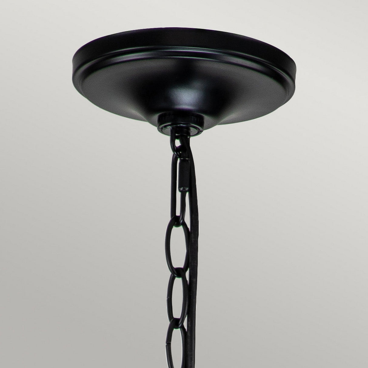 The Capitol Hill 6 Light Chandelier - Black showcases a black ceiling light fixture with a round canopy and linked chain, elegantly suspended against a simple gray backdrop.