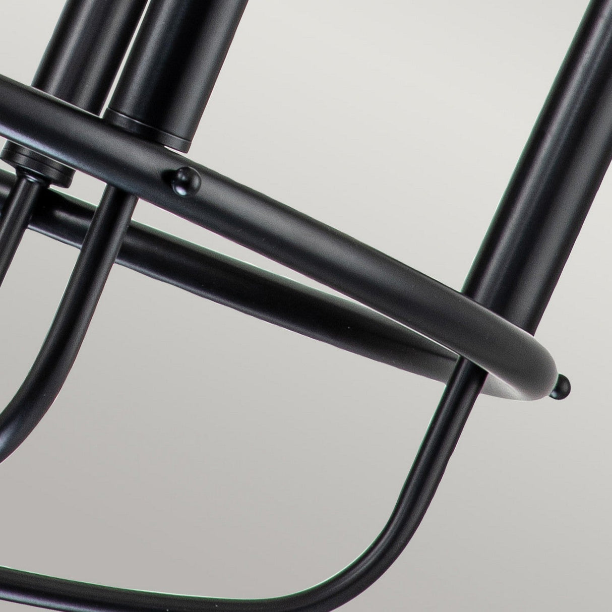 Close-up of the black metal frame from the Capitol Hill 6 Light Chandelier, highlighting interconnected cylindrical rods and smooth curved lines against a light gray background.