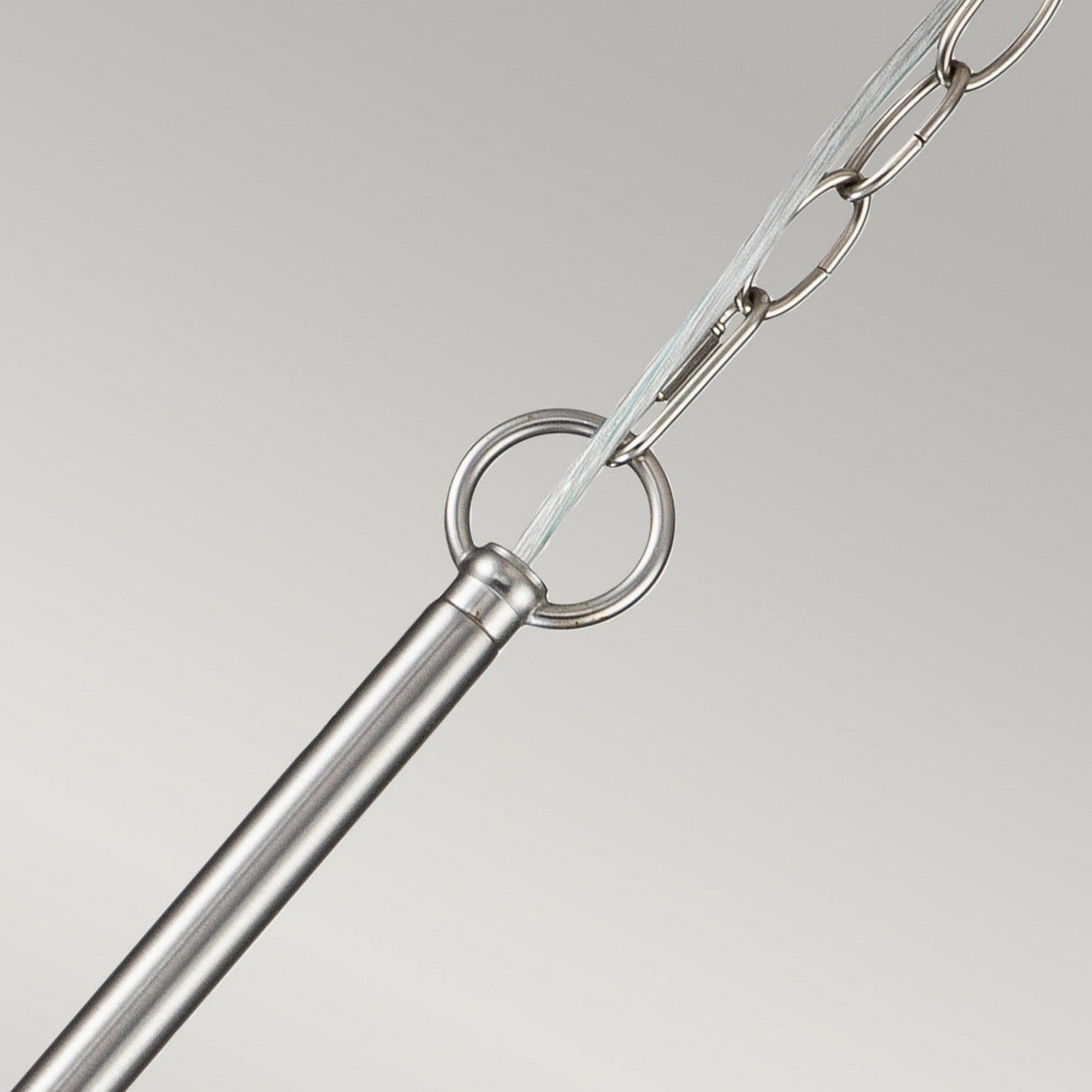 In the foreground, a detailed view of the Capitol Hill 6 Light Chandelier reveals its metal bar connected to a chain through a circular loop. The brushed nickel finish shines brightly, accentuated by ambient lighting against the simple backdrop, showcasing its elegant and polished design.