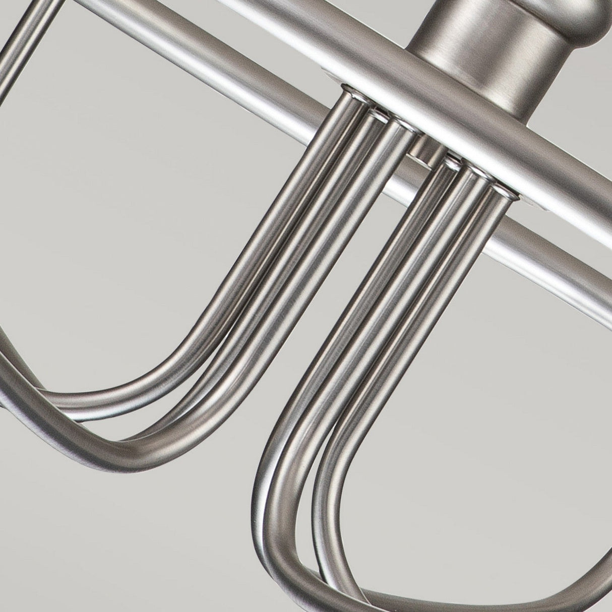 Close-up view of a Capitol Hill 6 Light Chandelier in brushed nickel, featuring several elegantly curved arms, gleaming under soft ambient lighting against a plain light-colored background.