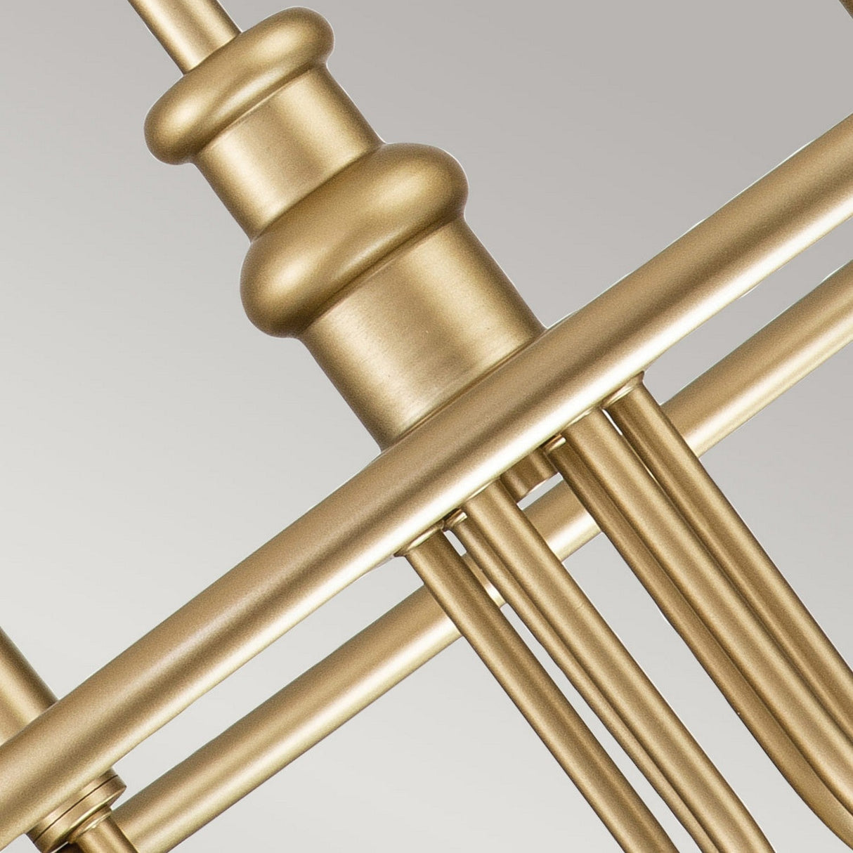 Close-up image of metallic gold rods and cylindrical components, reminiscent of the Capitol Hill 6 Light Chandelier - Natural Brass's refined design. Arranged in a geometric pattern, the sleek surfaces exude elegance against the soft gray background, echoing the warmth of natural brass.