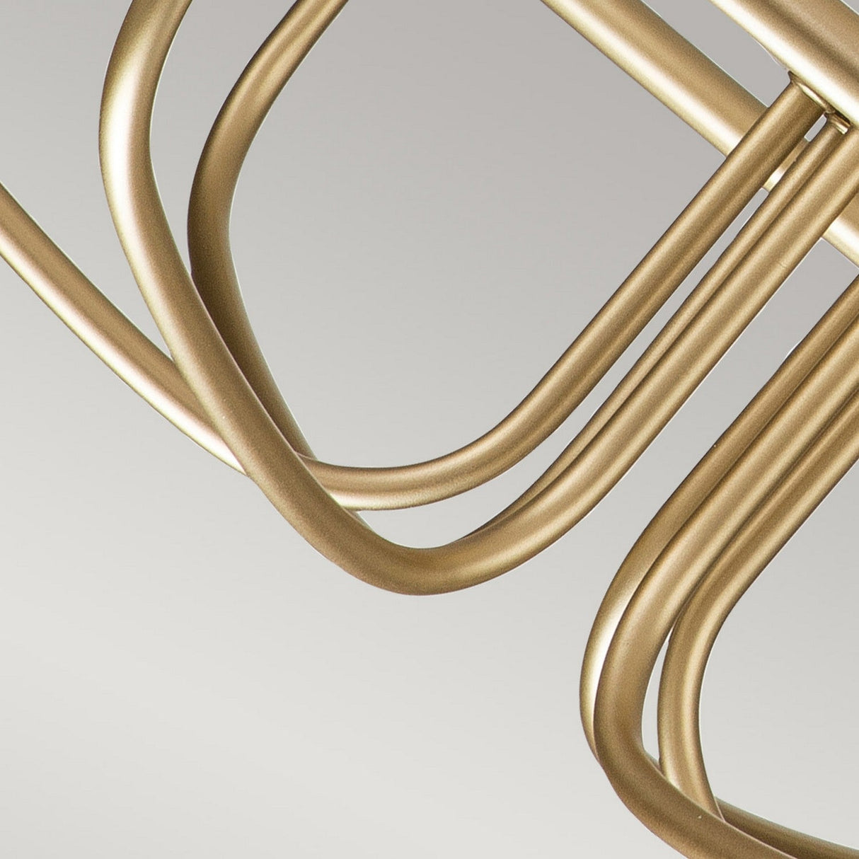 A close-up of a geometric sculpture made of interlocking, curved, natural brass tubes captures the elegance of the Capitol Hill 6 Light Chandelier - Natural Brass against a plain gray background.