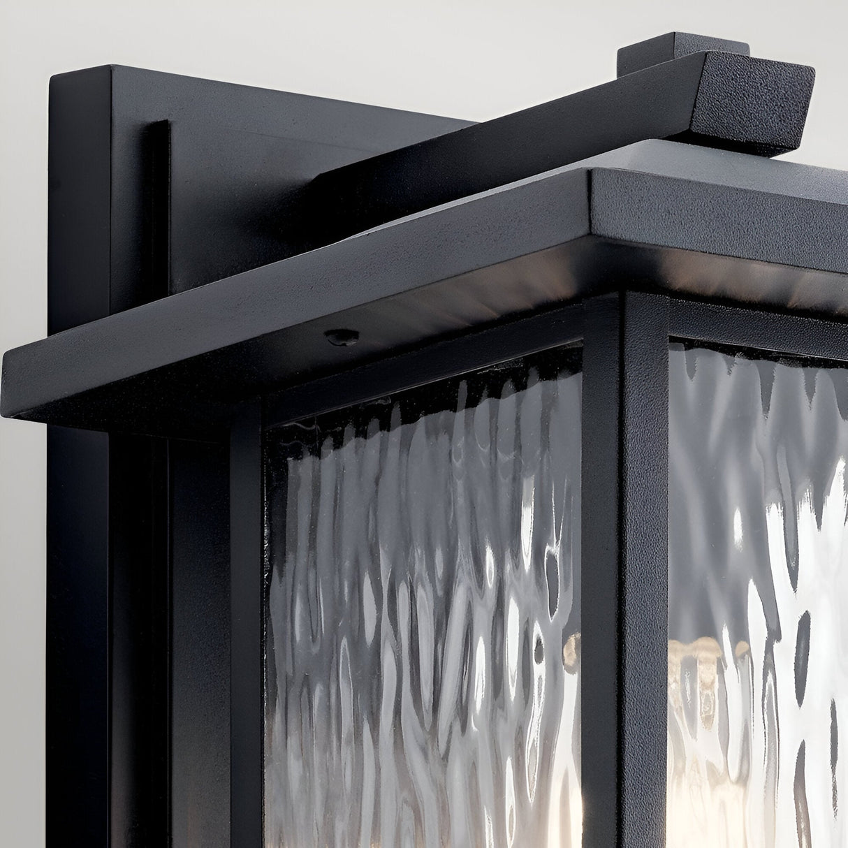 Close-up of the Cappanna 1 Light Outdoor Medium Wall Lantern in Textured Black, featuring a rectangular frame and waterfall glass panels, mounted on a light-colored wall.
