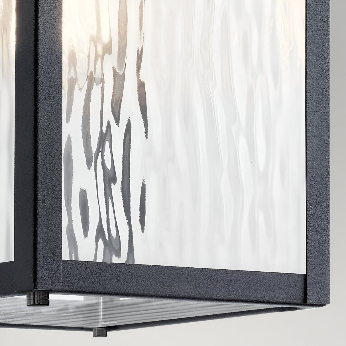 Close-up of the Cappanna 1 Light Outdoor Medium Wall Lantern in textured black, showcasing its waterfall glass panels framed by a matte black, weather-resistant metal border against a light background.