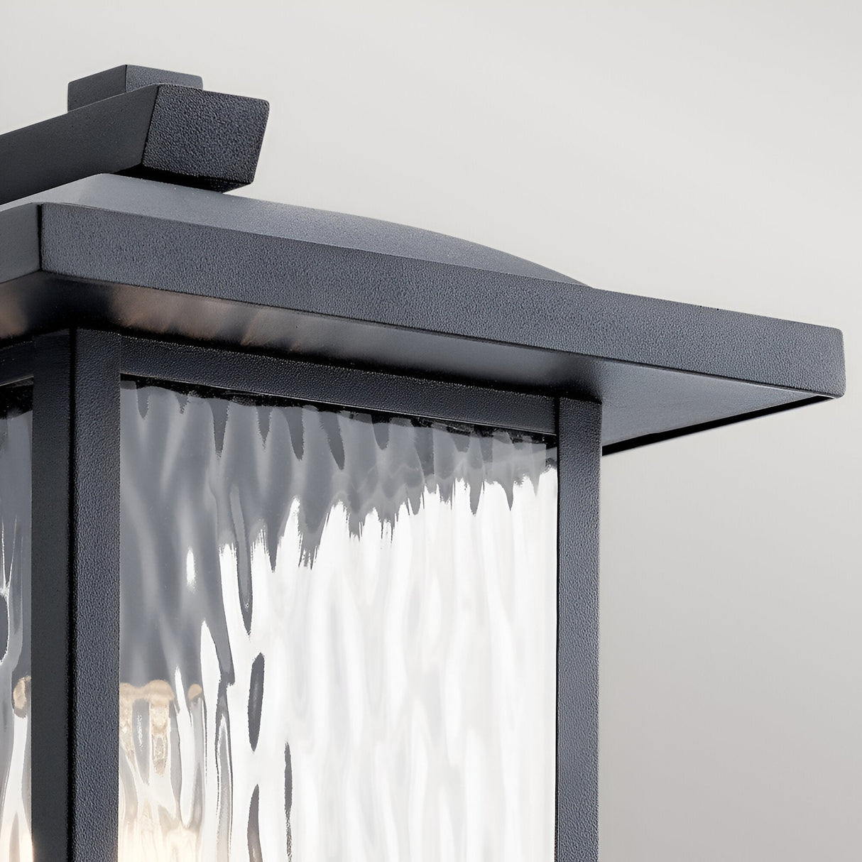 Close-up of the Cappanna 1 Light Outdoor Medium Wall Lantern in textured black, featuring a weather-resistant waterfall glass panel and mounted on a light gray background.