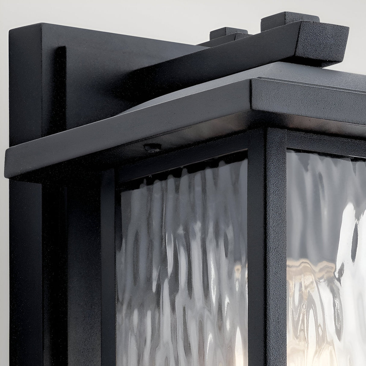 Close-up of the Cappanna 1 Light Outdoor Small Wall Lantern in textured black, with waterfall glass panels and clean angular lines, mounted on a light wall—an ideal choice for modern, stylish outdoor lighting.