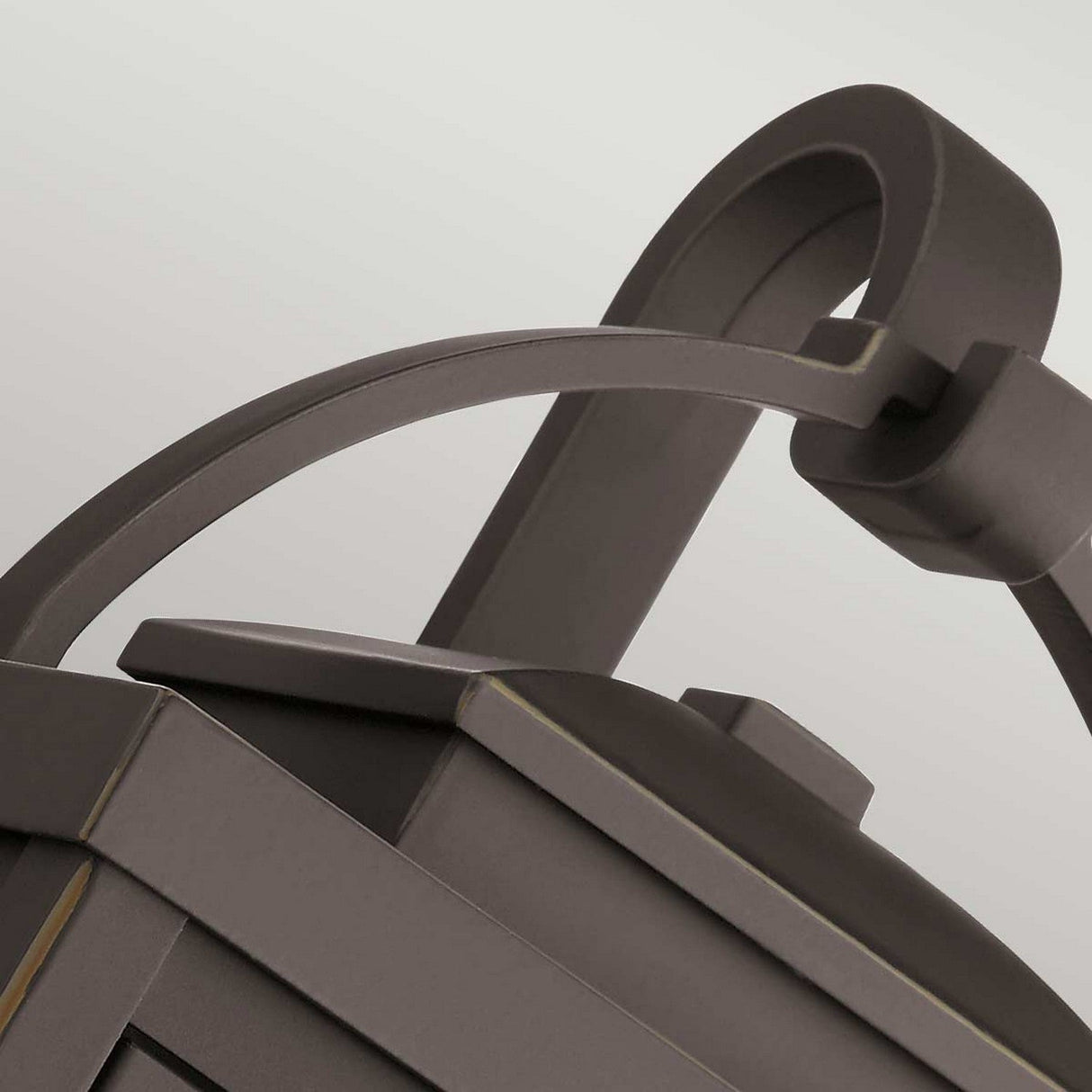 Close-up of the Carlson Outdoor 2 Light Wall Lantern in rubbed bronze, showcasing its sleek and modern design. The lantern features a curved handle and smooth geometric lines against a light grey background, accented with subtle metallic details and a minimalist aesthetic. Its seeded glass adds an extra touch of elegance.