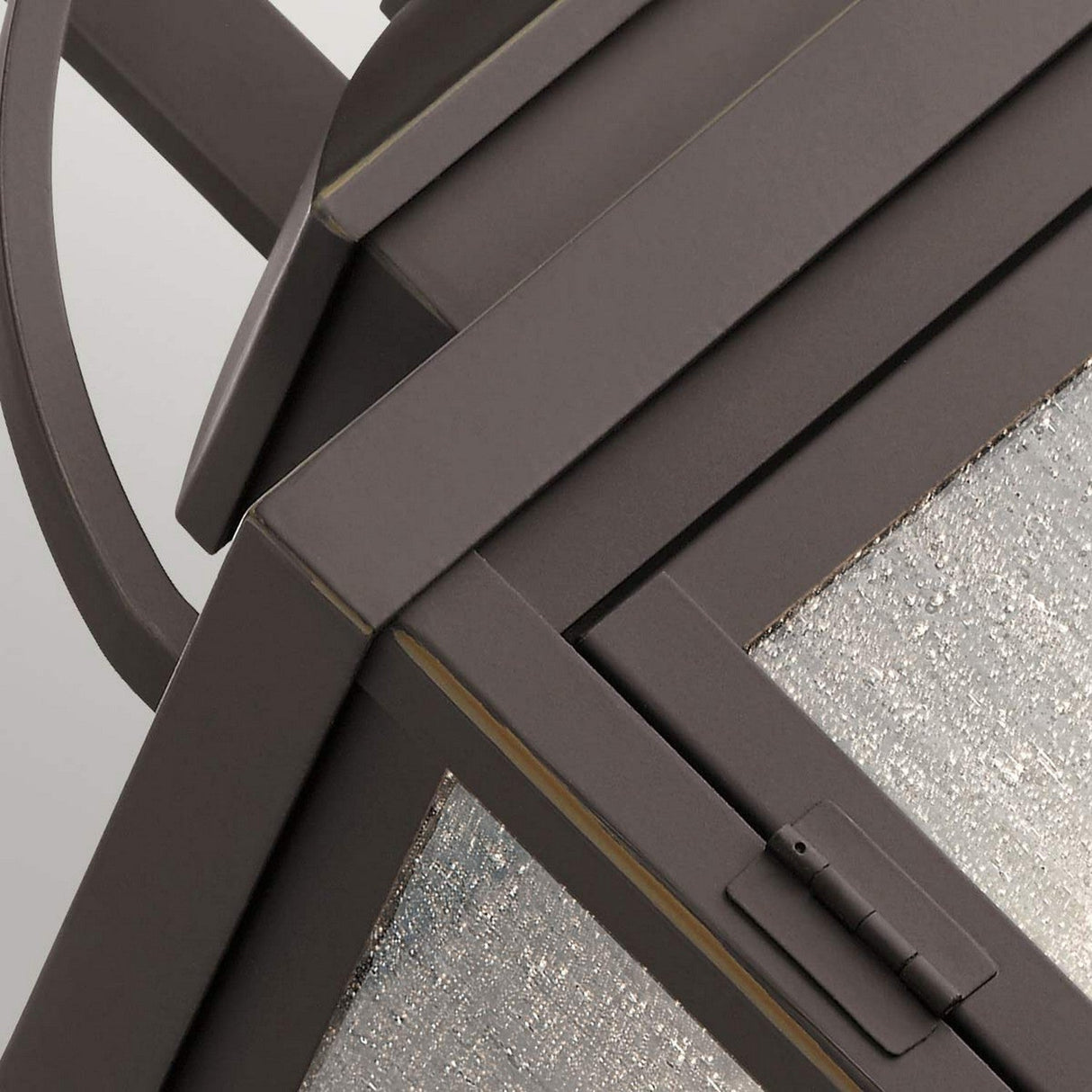 Close-up of the Carlson Outdoor 2 Light Wall Lantern with a sophisticated geometric design featuring a metal frame and seeded glass panels. It showcases sharp angles and boasts a sleek, industrial aesthetic reminiscent of an outdoor lantern in rubbed bronze.