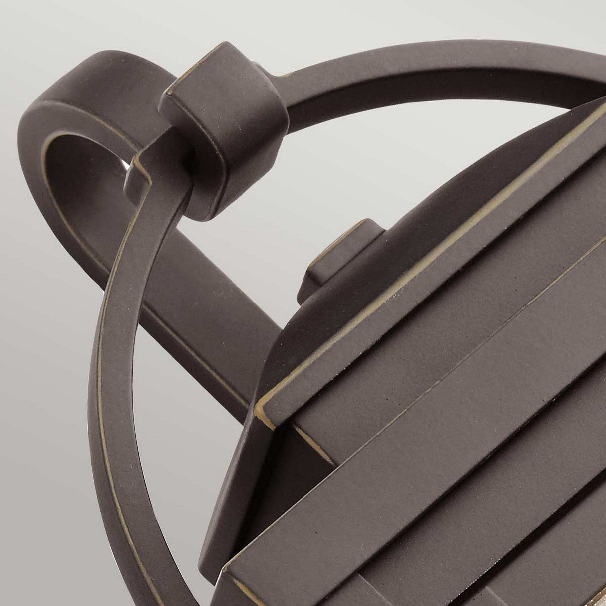 Close-up of the Carlson Outdoor 1 Light Wall Lantern in a modern, matte black finish showcasing a geometric design. The lantern features sleek lines, an angled top, and includes accents of rubbed bronze along with seeded glass details, all set against a light gray background.