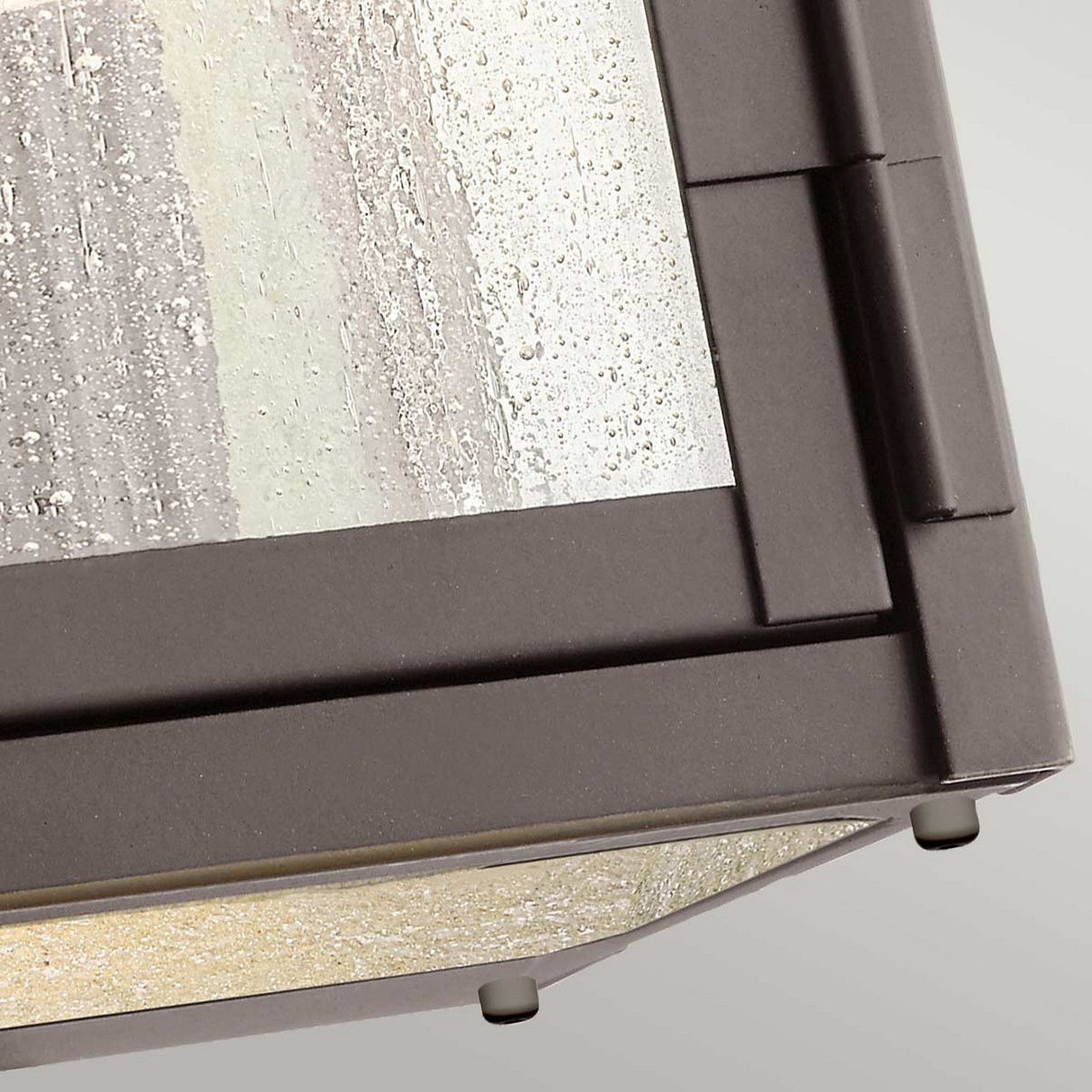 Close-up of the Carlson Outdoor 1 Light Wall Lantern in rubbed bronze, showcasing its geometric design and seeded glass panels against a neutral background.