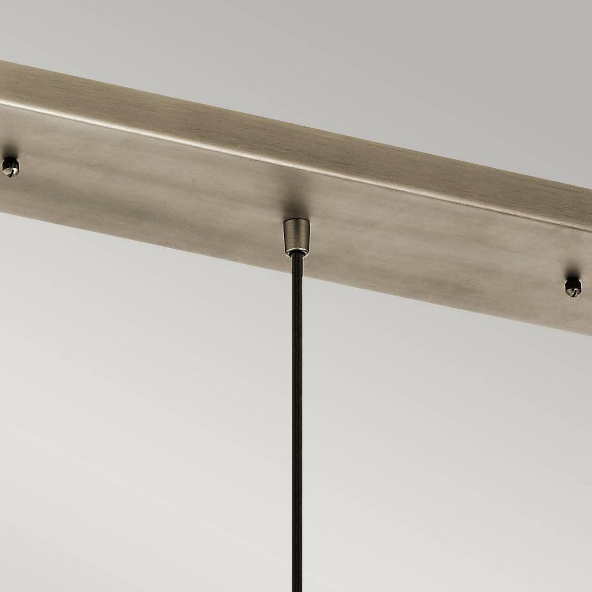 A close-up view highlights the elegant design of a ceiling-mounted light fixture, featuring the Ceiling Pan Rectangular Ceiling Plate in a sleek silver finish. A single thin rod extends from this rectangular plate, securely attached to the ceiling against a plain gray background, reminiscent of modern mini-pendant lights.