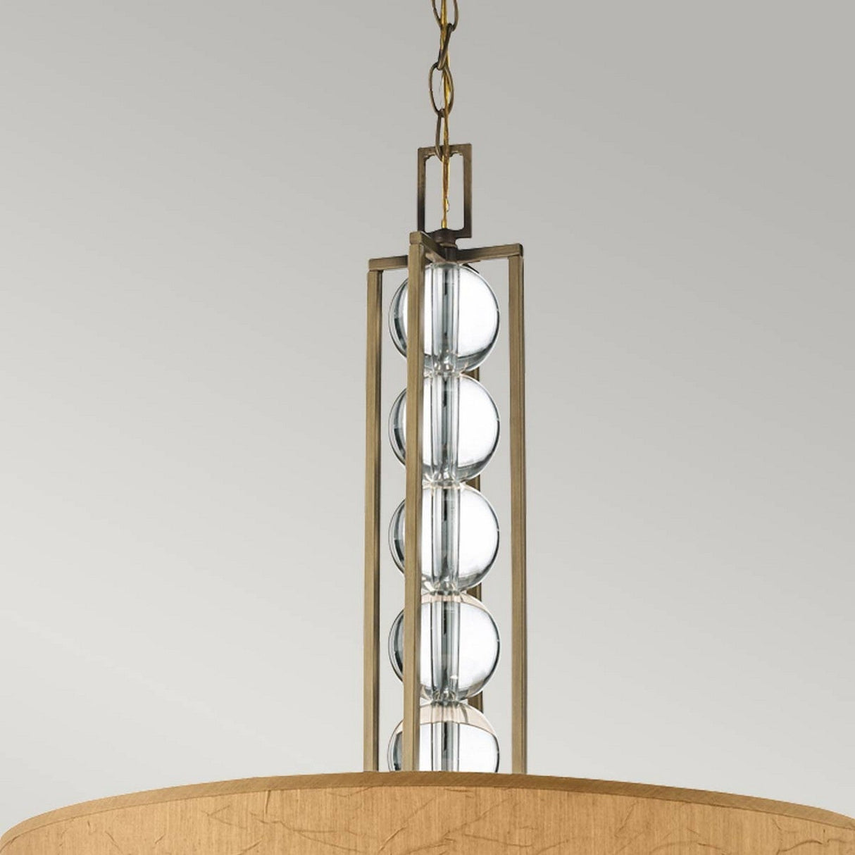 The Celestial 3 Light Pendant - Bronze is a contemporary hanging fixture featuring a cylindrical wooden shade and a decorative bronze rod adorned with multiple optical crystal spheres. It is elegantly suspended from a metal chain against a plain gray background.