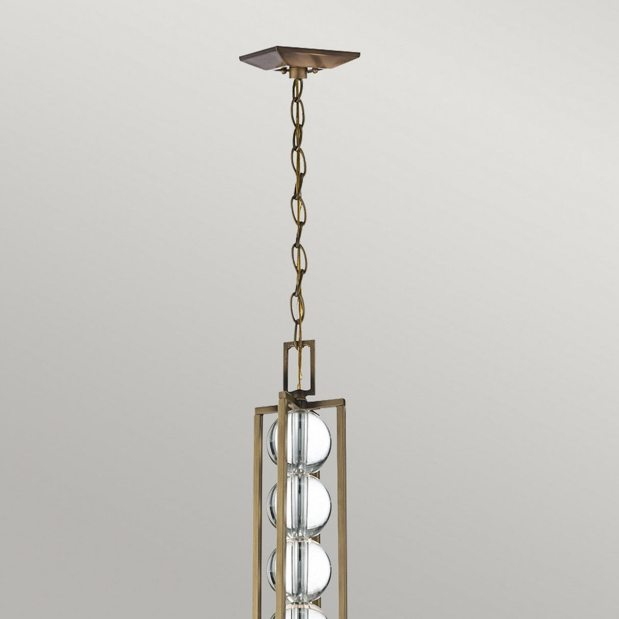 The Celestial 3 Light Pendant - Bronze features a modern geometric frame suspended from the ceiling by a chain. Its bronze structure encases optical crystal spheres, adding sophistication and style that enhances any space.