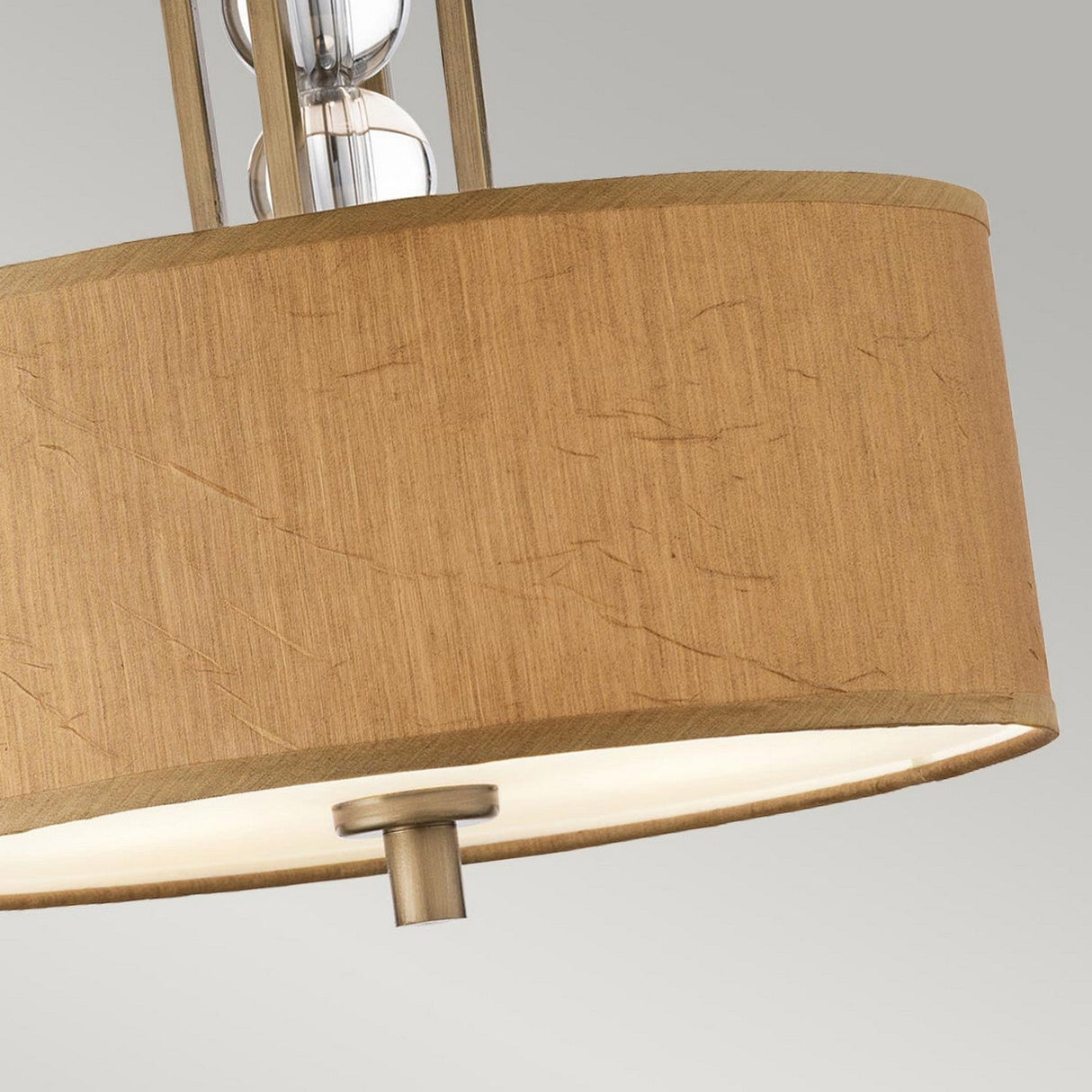 Close-up of the Celestial 3 Light Semi Flush - Bronze lamp with a cylindrical, textured beige lampshade. The semi-flush design highlights its bronze metal frame, featuring three exposed bulbs inside. The celestial-inspired piece stands against a simple light gray background.