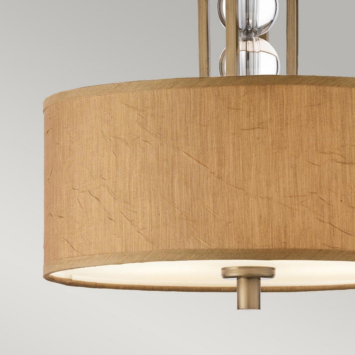 An up-close view of the Celestial 3 Light Semi Flush - Bronze showcases a cylindrical beige fabric shade paired with a bronze metallic rod. The semi-flush fixture features an elegant, clear celestial neck and is stunningly displayed against a neutral gray background.