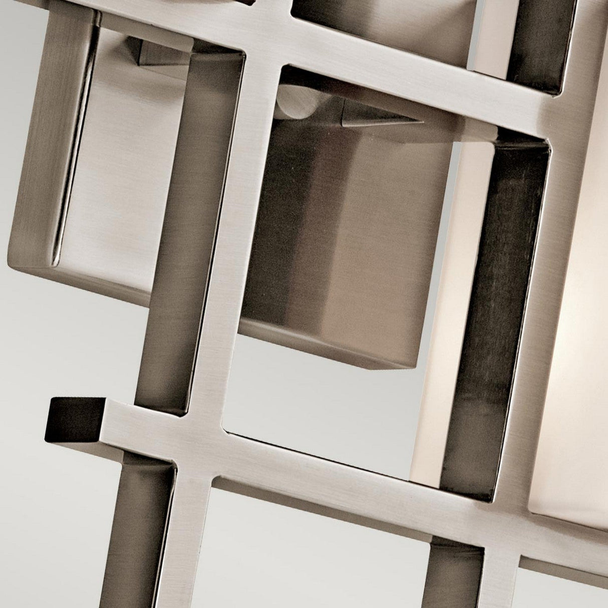 Close-up of the City Lights 2 Light Wall Light - Silver, featuring a modern geometric metal grille with square and rectangular openings that embody a contemporary style. Its reflective surface showcases a sleek silver metallic finish, subtly enhanced by integrated LED technology. A softly blurred background adds to its elegant appeal.