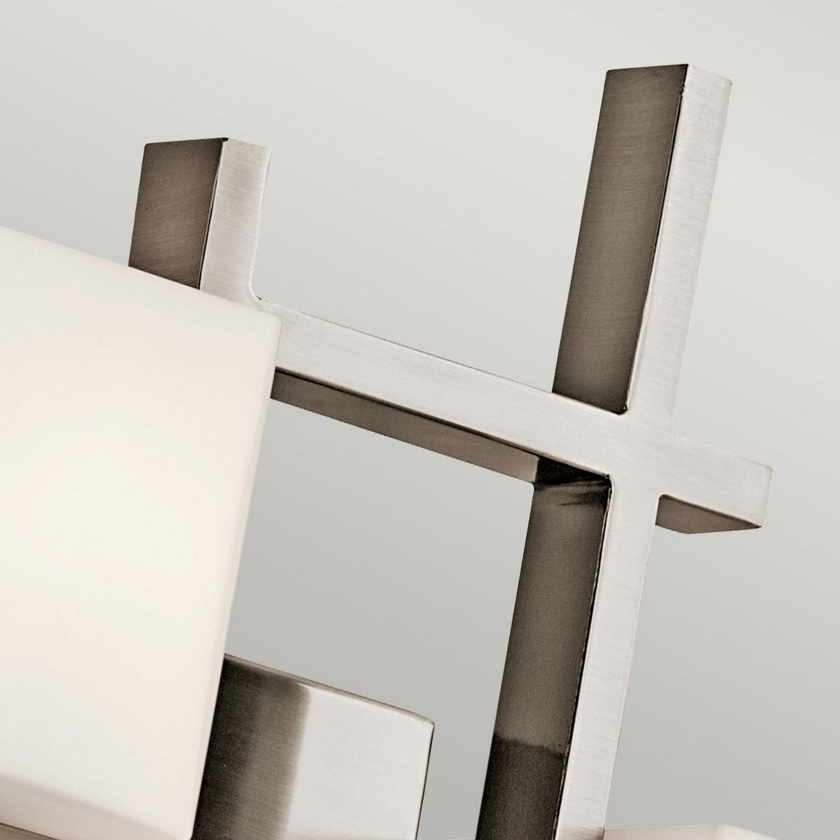 Close-up of the City Lights 2 Light Wall Light in silver, showcasing intersecting polished metal elements and geometric shapes illuminated by subtle LED technology against a neutral background.