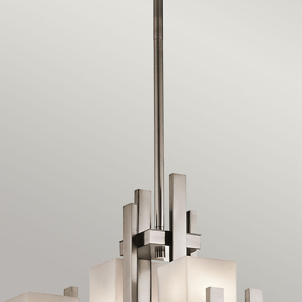 The City Lights 7 Light Chandelier - Silver exudes sophistication with its sleek metallic structure, featuring LED lighting and multiple rectangular frosted glass shades, elegantly suspended from a lengthy rod against a plain background.