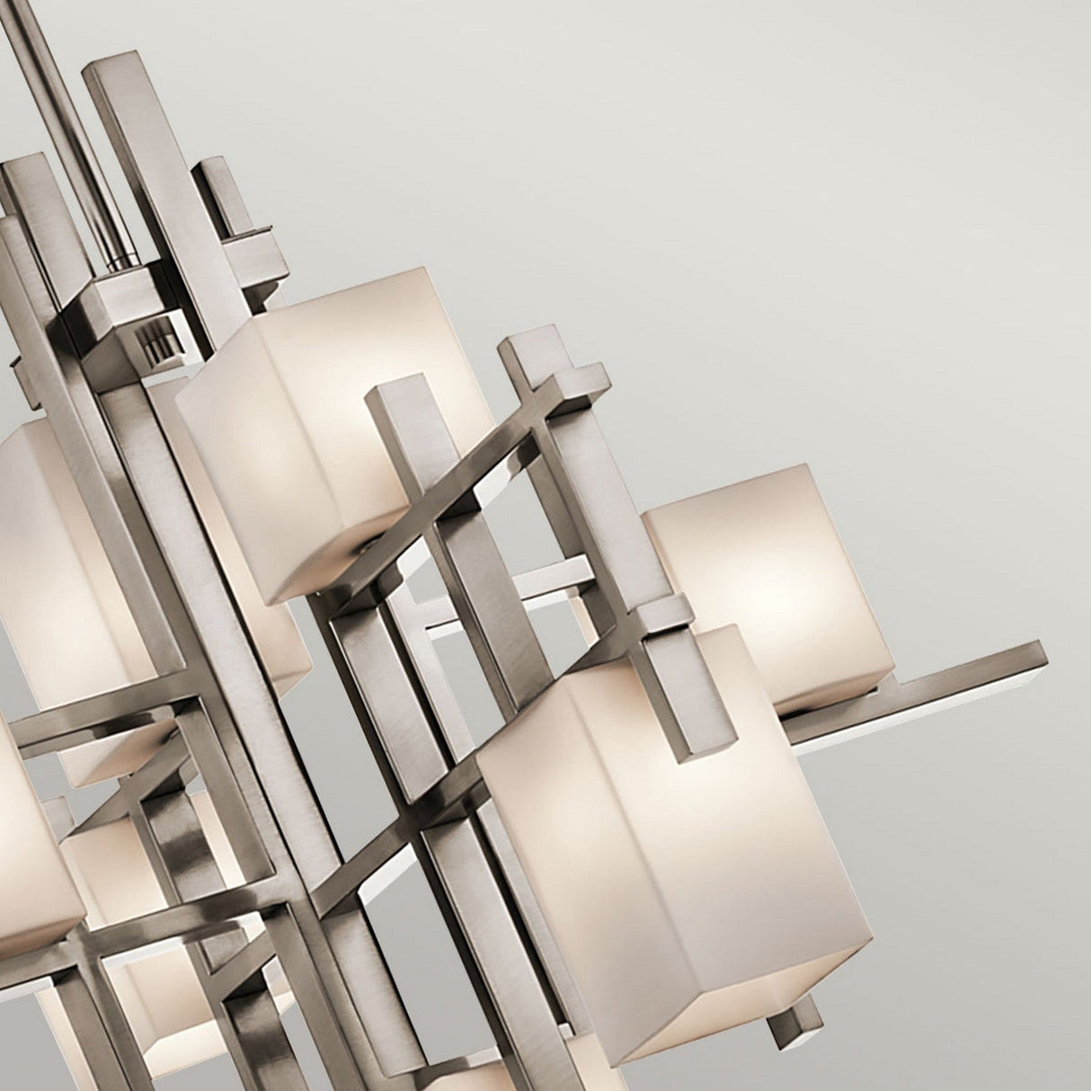 Close-up of the City Lights 7 Light Chandelier in Silver, showcasing a striking geometric pattern. It features intersecting metal rods and cube-shaped frosted glass shades, each housing warm LED lights. The background offers a soft, neutral color that enhances its contemporary allure.