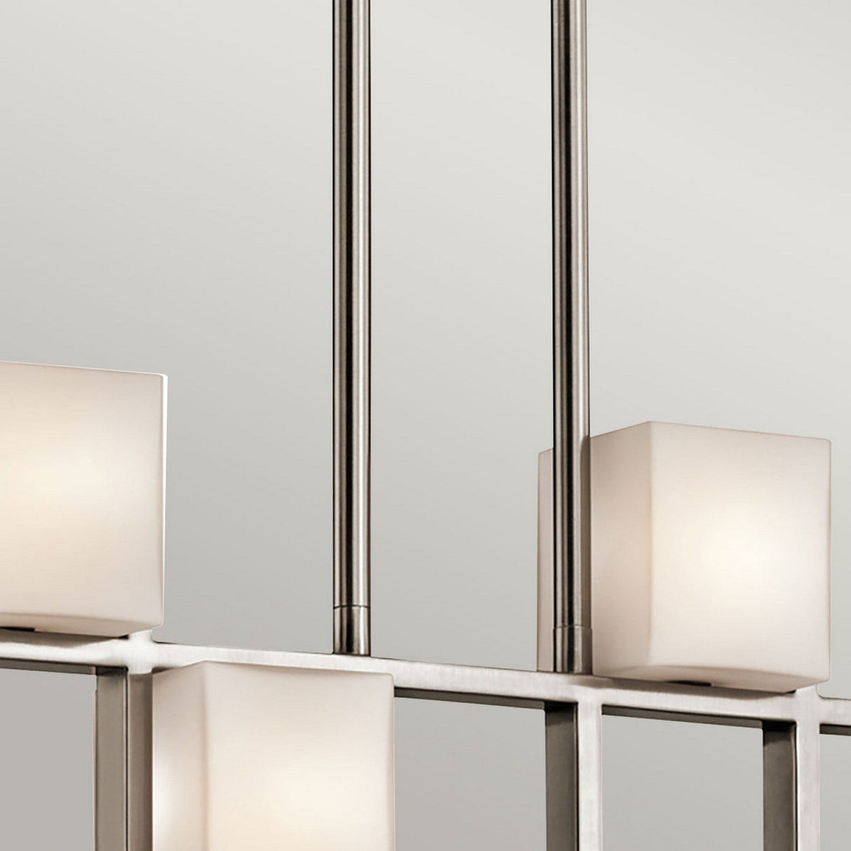 The City Lights 7 Light Linear Chandelier in silver showcases rectangular, frosted glass shades on sleek metal rods against a light gray background. Its design embodies clean lines and a minimalist style, further enhanced by energy-efficient LED lights for the ultimate modern decor.