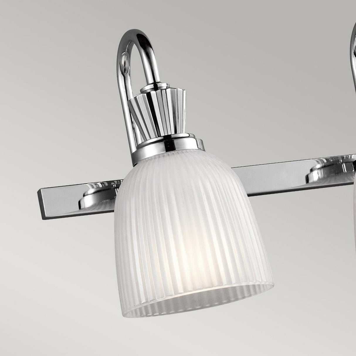 The Cora 4 Light Wall Light in polished chrome showcases a contemporary curved design, ideal for bathroom lighting. Its vertical ribbed glass shade diffuses a gentle light from LED lamps, all elegantly mounted on a rectangular base.