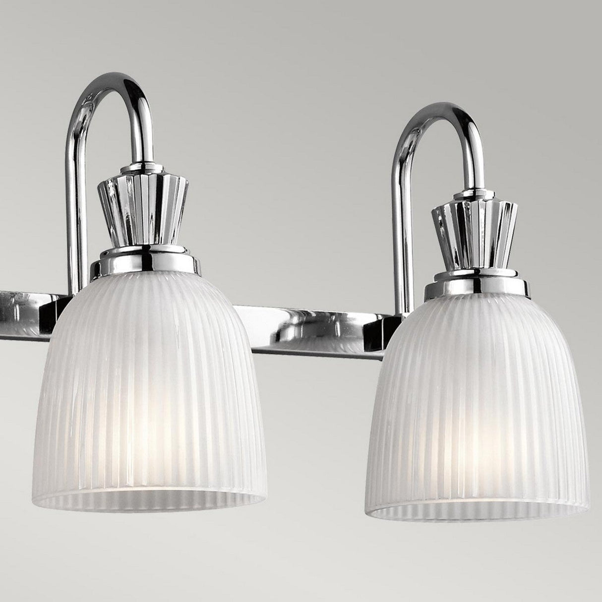 The Cora 4 Light Wall Light in polished chrome features ribbed frosted glass shades and showcases curved arms with elegant detailing. It's mounted on a rectangular backplate, making it ideal for bathroom lighting against a neutral background.