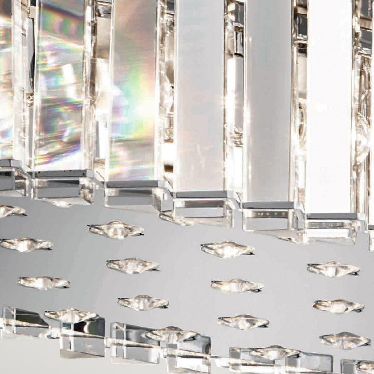 A close-up of the Crystal Skye 12 Light Island Chandelier - Chrome showcases its modern design, featuring vertical glass prisms that reflect light and create stunning rainbow patterns. The sleek chrome finish enhances the elegance of this fixture.