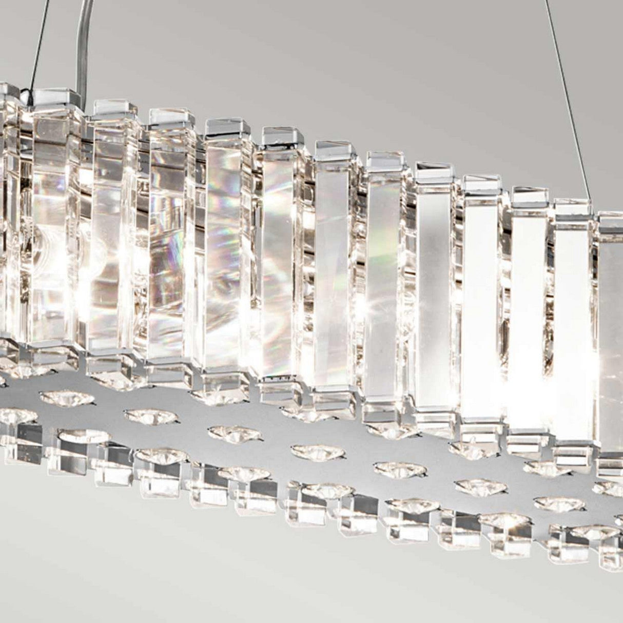 A close-up of the Crystal Skye 8 Light Island Chandelier in Chrome highlights its modern elegance with vertical rectangular crystal prisms that beautifully reflect light. Set against a soft, neutral background, its shimmering effect is enhanced while providing energy-efficient lighting for a sustainable touch.