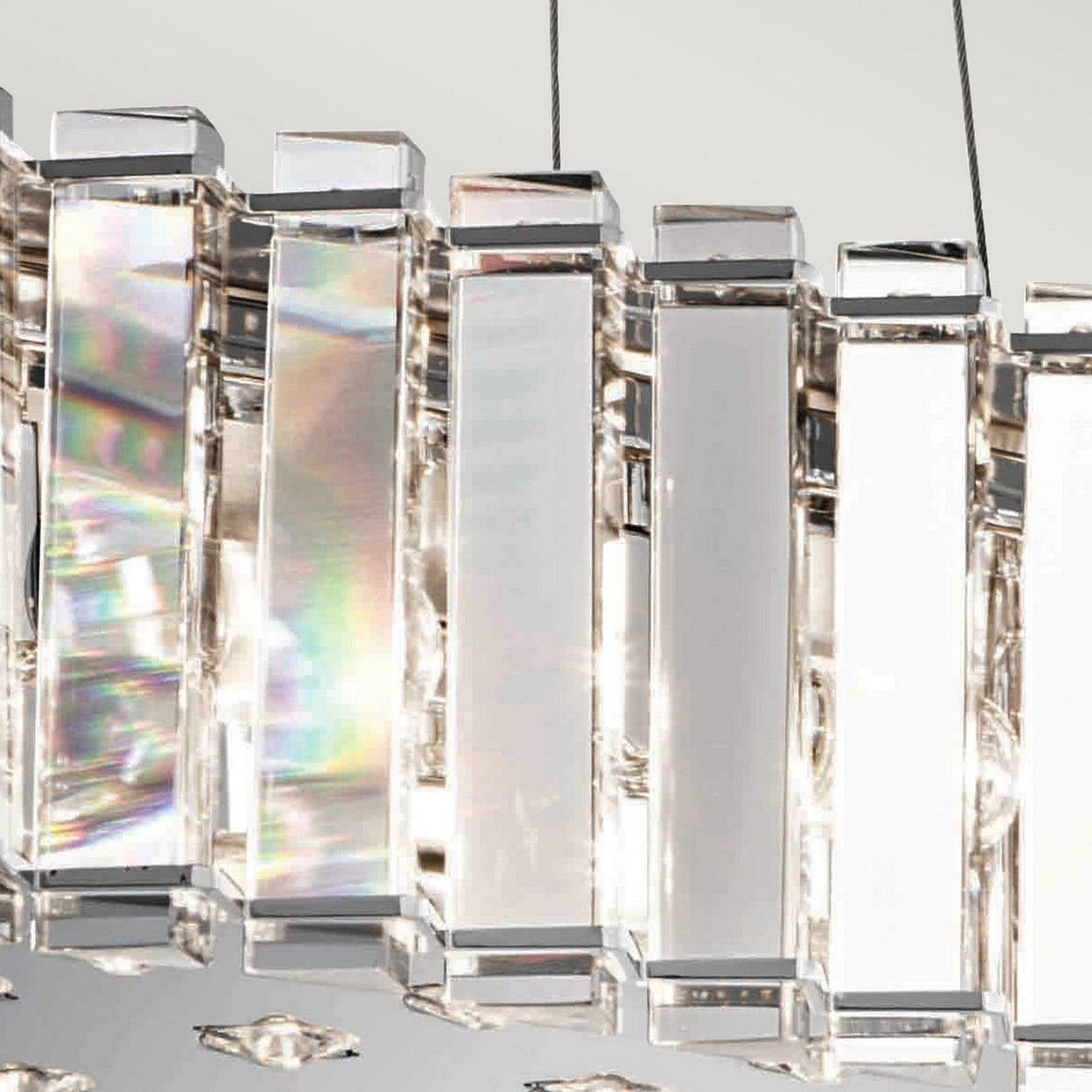 A close-up of the Crystal Skye 8 Light Island Chandelier - Chrome reveals rectangular glass prisms that reflect light, producing a spectrum of colors and a shimmering effect. The design captures modern elegance against a soft, neutral background while emphasizing its energy-efficient lighting.