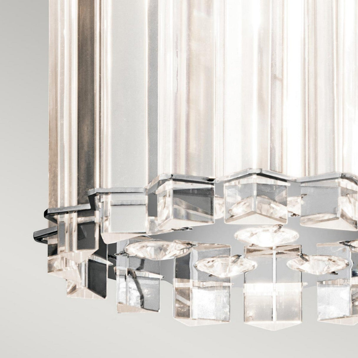 A close-up of the Crystal Skye 2 Light Mini Pendant in chrome showcases its modern design, featuring angular, prism-like pieces that beautifully reflect light. The chrome accents emphasize its geometric style against a soft gray background, while the transparent crystal prisms bring an elegant touch to this mini pendant piece.