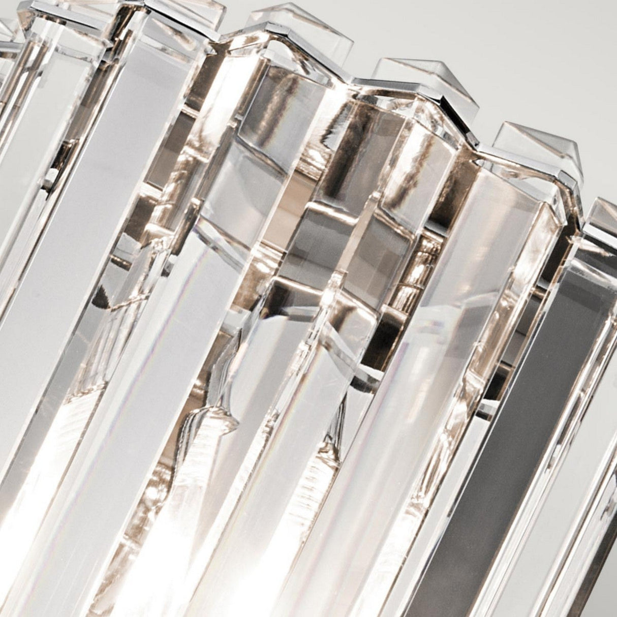 Close-up of a modern Crystal Skye 2 Light Wall Light highlighted by Chrome details and multiple vertical, clear glass prisms. The prisms catch and reflect light, generating a sparkling effect. The overall tone is clean and elegant.