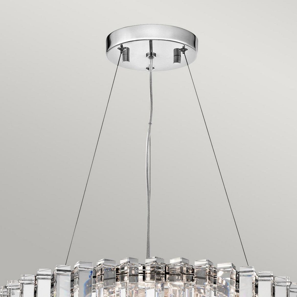 The Crystal Skye 8 Light Chandelier - Chrome is a masterpiece of luxury lighting, suspended by three cables. It showcases multiple vertical, triangular crystal prisms that beautifully reflect light. The ceiling mount is circular and metallic, perfectly complementing the elegant design.