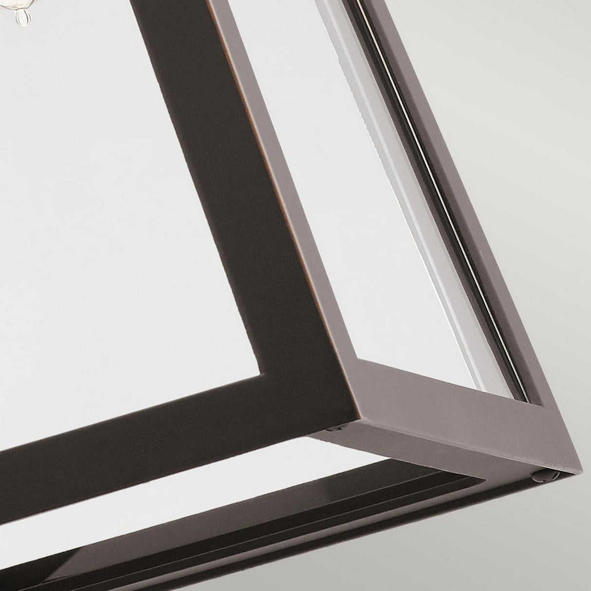 A close-up of the Delison Outdoor 1 Light Wall Lantern reveals its modern geometric design, featuring a sleek rubbed bronze metal frame and clear glass panels. Elegantly suspended, this IP44-rated fixture is perfect for illuminating the rustic lodge exterior while highlighting its sharp edges and minimalist charm.