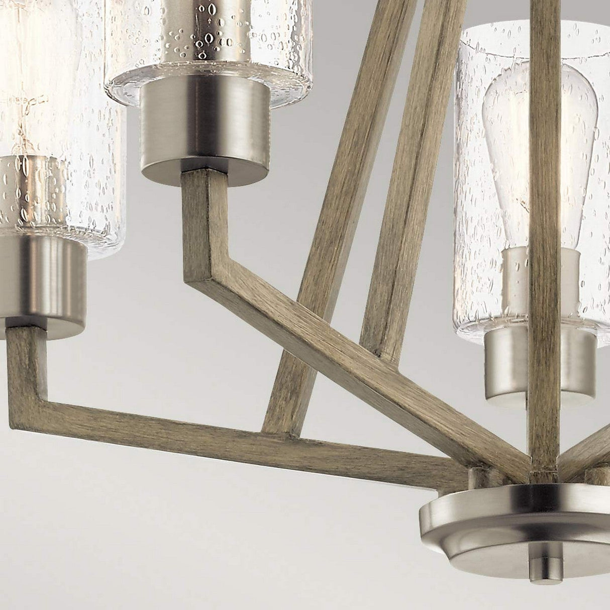 The Deryn 5 Light Chandelier - Antique Grey captures rustic allure with its wood and metal structure, featuring five textured glass shades. The visible bulbs accentuate its contemporary charm, echoing a sleek design.