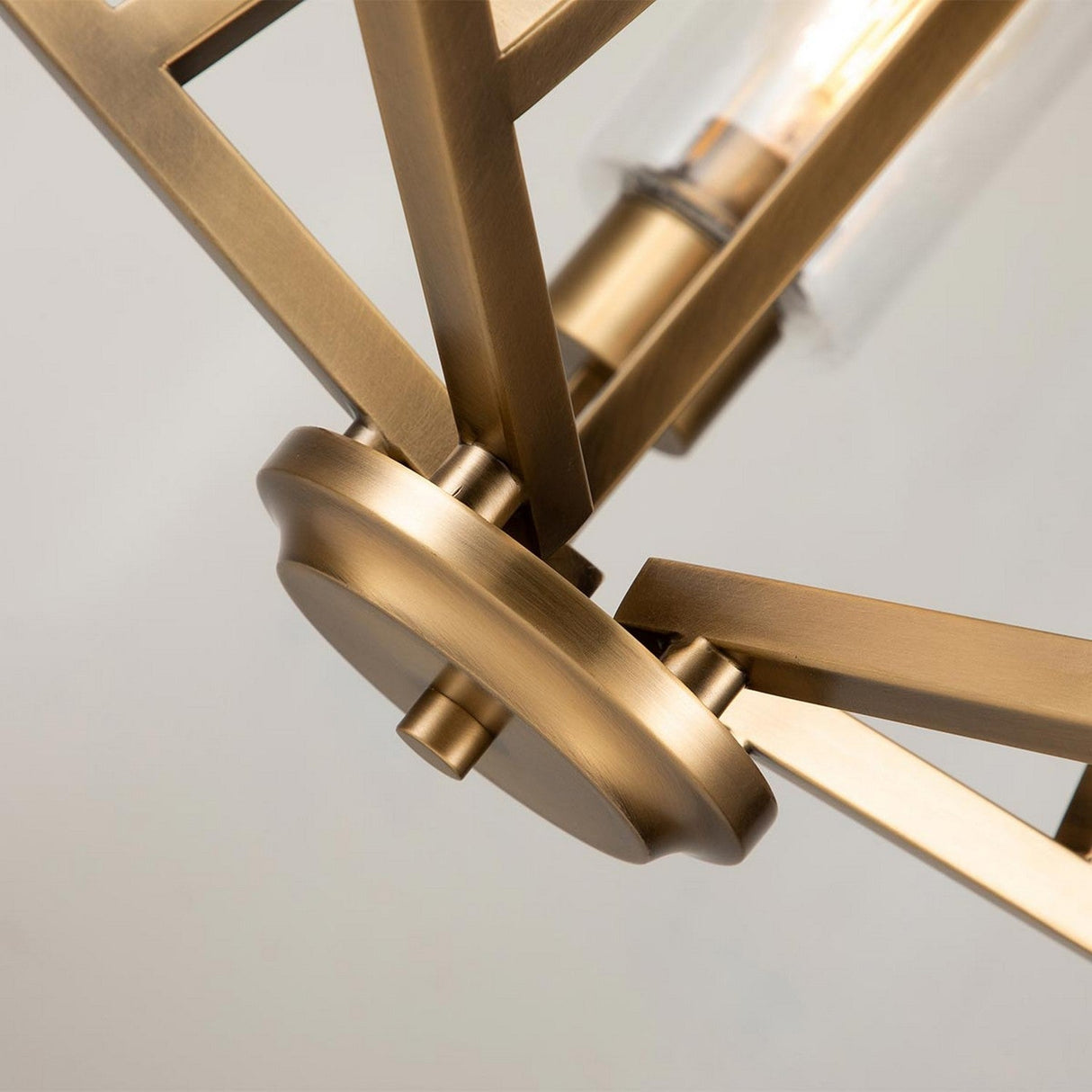 Close-up of the Deryn 5 Light Chandelier in natural brass, featuring angular metal arms and seeded glass accents, set against a neutral background. The design showcases sleek geometric lines and a warm metallic finish.