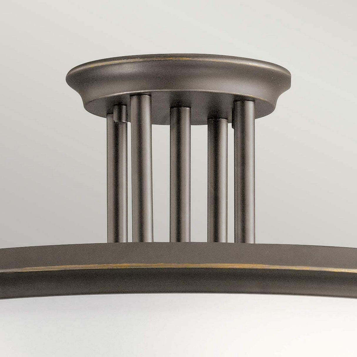 A close-up of the Dreyfus 3 Light Semi Flush showcases its Olde Bronze finish, featuring a circular base with four vertical rods that connect to a shallow frosted glass dome shade, highlighted by an optical crystal accent for a sleek and industrial design.